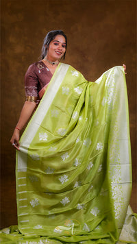 Woman wearing a green saree with a white border against a brown background