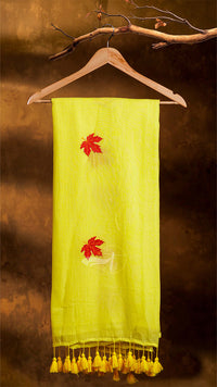 Yellow scarf with red leaf designs and tassels on a wooden hanger against a brown background