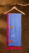 Blue scarf with pink border and tassels hanging on a wooden hanger against a brown background.