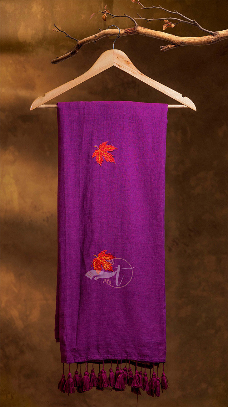 Purple scarf with embroidered designs on a wooden hanger against a brown background