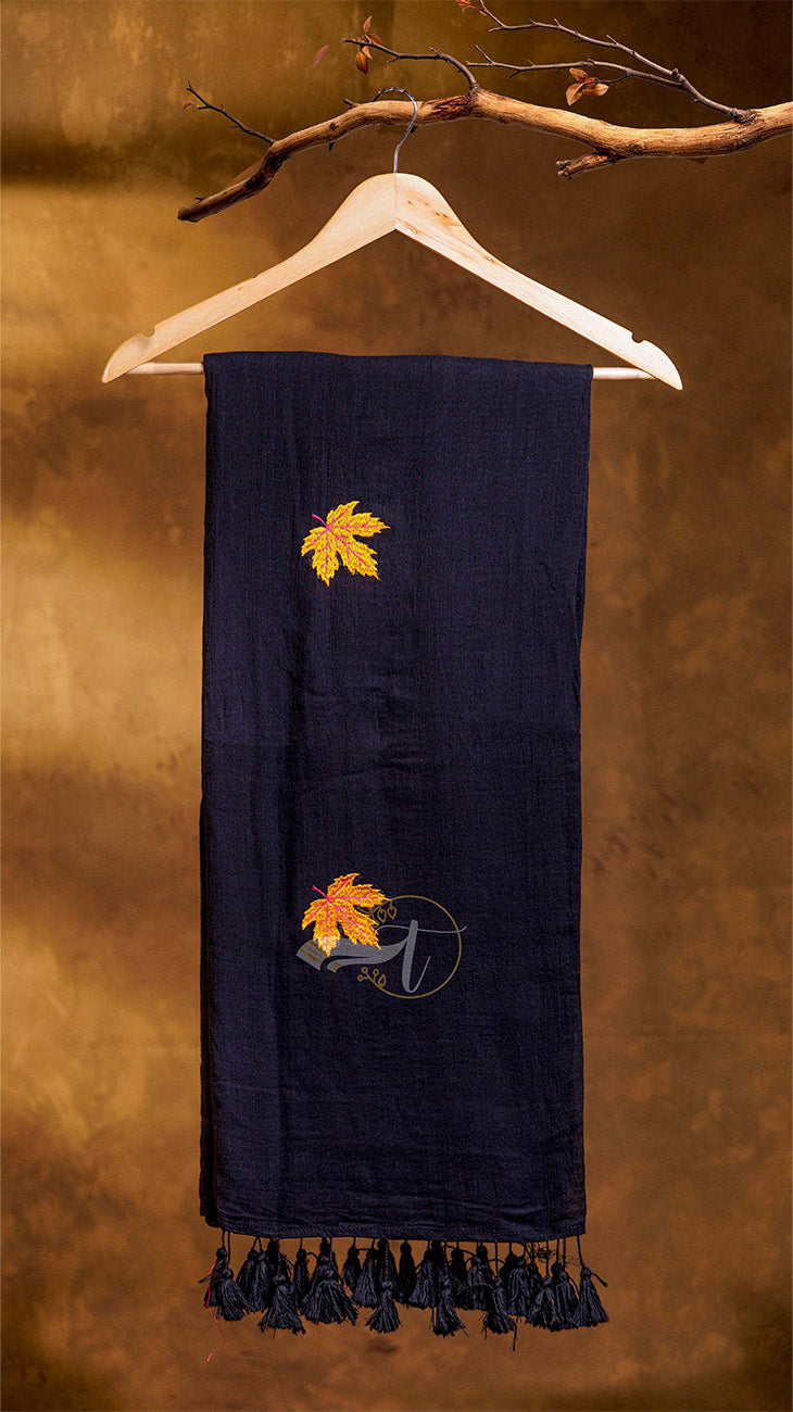 Navy blue scarf with embroidered leaf design on a wooden hanger against a brown background