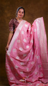 Woman wearing a pink saree with white patterns against a brown background