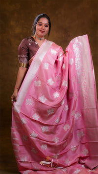Woman wearing a pink saree with white patterns against a brown background