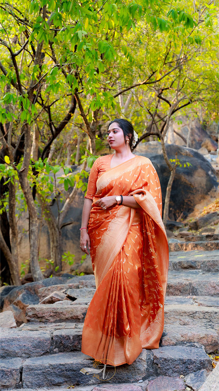 Woman in an orange saree standing on stone steps with greenery in the background