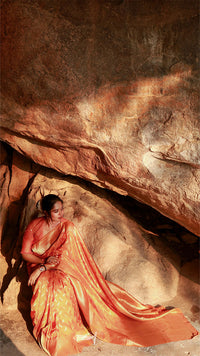 Woman in an orange saree sitting on a rocky surface