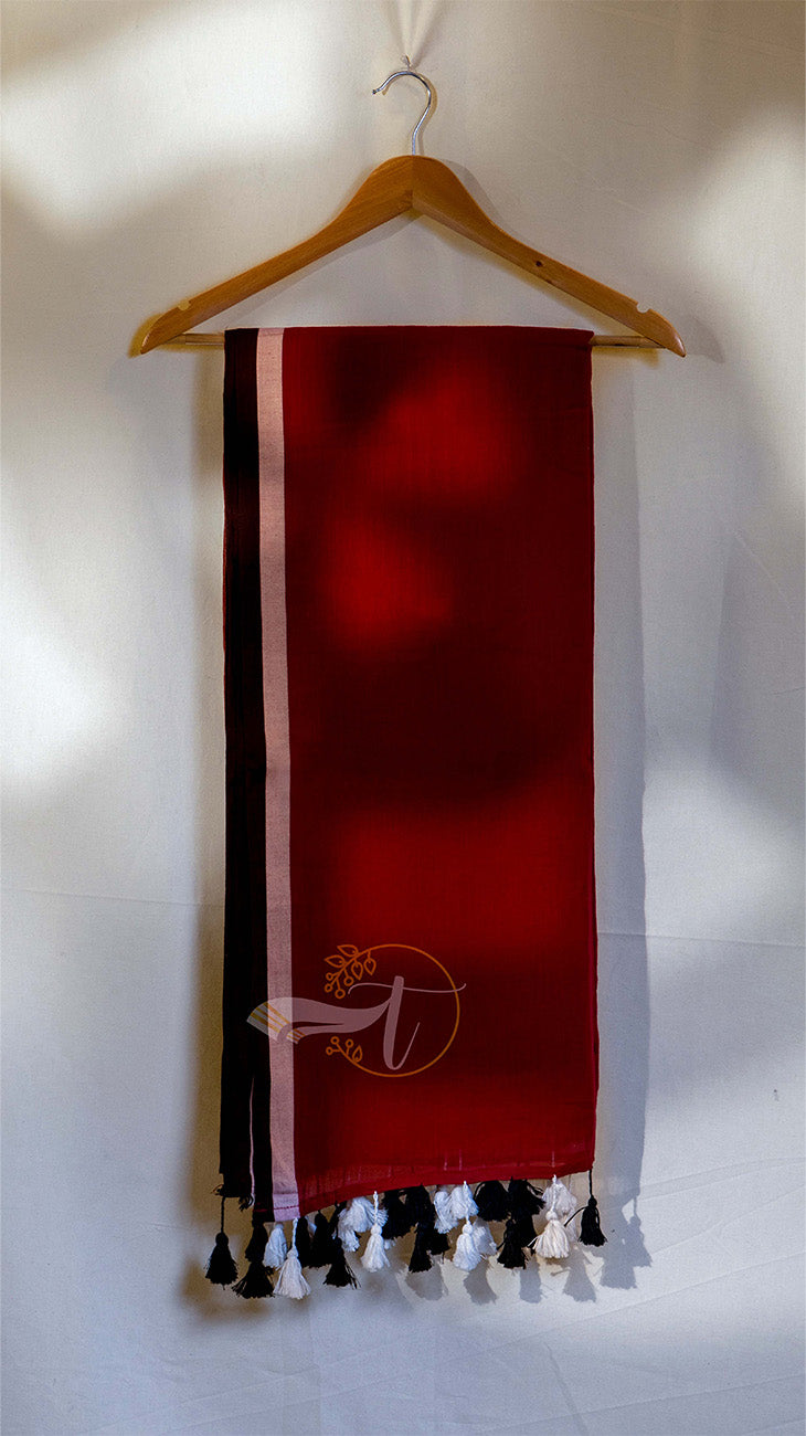 Red scarf with black and white tassels on a wooden hanger against a white wall.