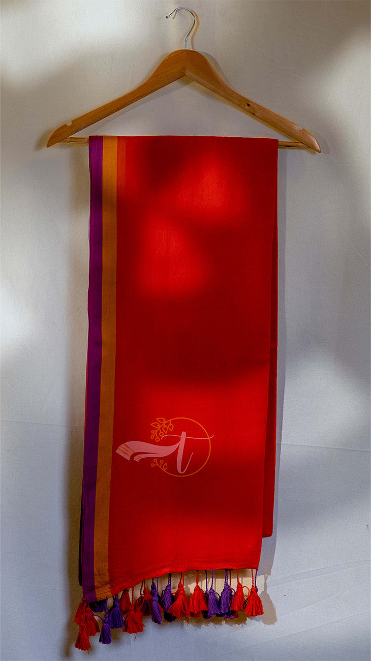Red scarf with purple and yellow stripes hanging on a wooden hanger against a white wall.