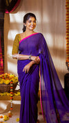 Woman in a purple saree with a yellow blouse standing indoors.