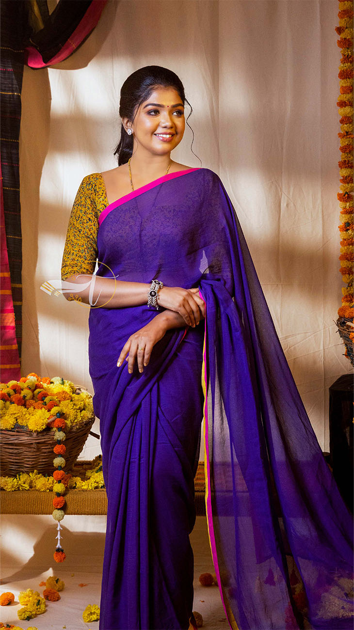 Woman in a purple saree with a yellow blouse standing indoors.