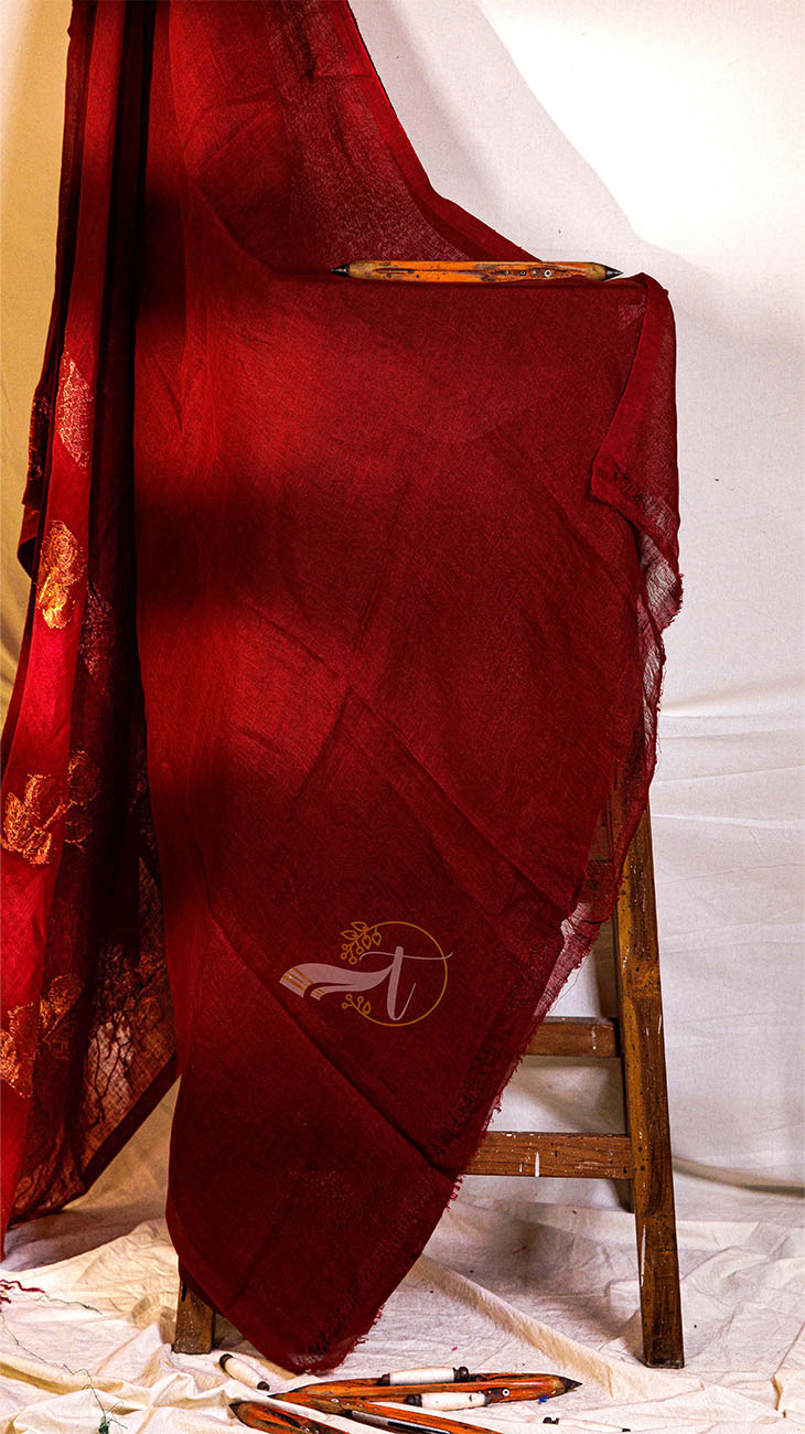 Red fabric with gold patterns draped over a wooden chair against a white background