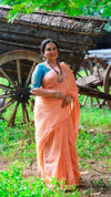 Woman in a peach saree standing in a natural setting with wooden carts in the background