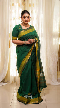 Woman wearing a green saree with a yellow border against a white curtain background