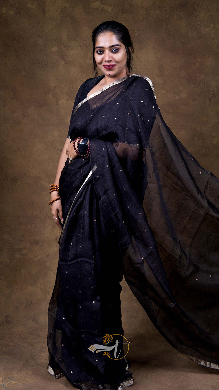 Woman wearing a black saree with a gold border against a brown background