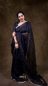 Woman wearing a black saree with a plain background