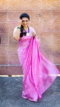 Woman in a pink saree standing against a textured wall.