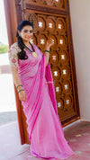 Woman in a pink saree standing in front of a decorative wooden door.