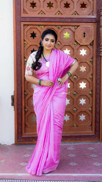 Woman in a pink saree standing in front of an ornate wooden door.