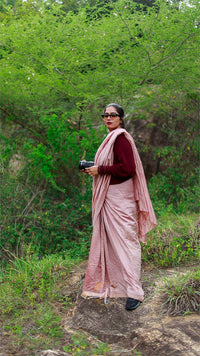 Woman in a pink saree standing in a forested area