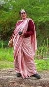 Woman in a pink saree standing outdoors with greenery in the background