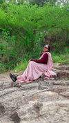 Woman in a pink saree sitting on rocks with greenery in the background