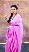 Woman in a pink saree standing against a textured wall.