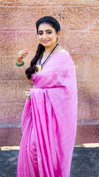 Woman in a pink saree standing against a textured wall.